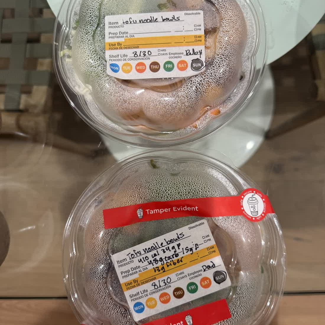 Two clear domed bowls of tofu noodles, a label on each, the lower one sealed with a red tamper band