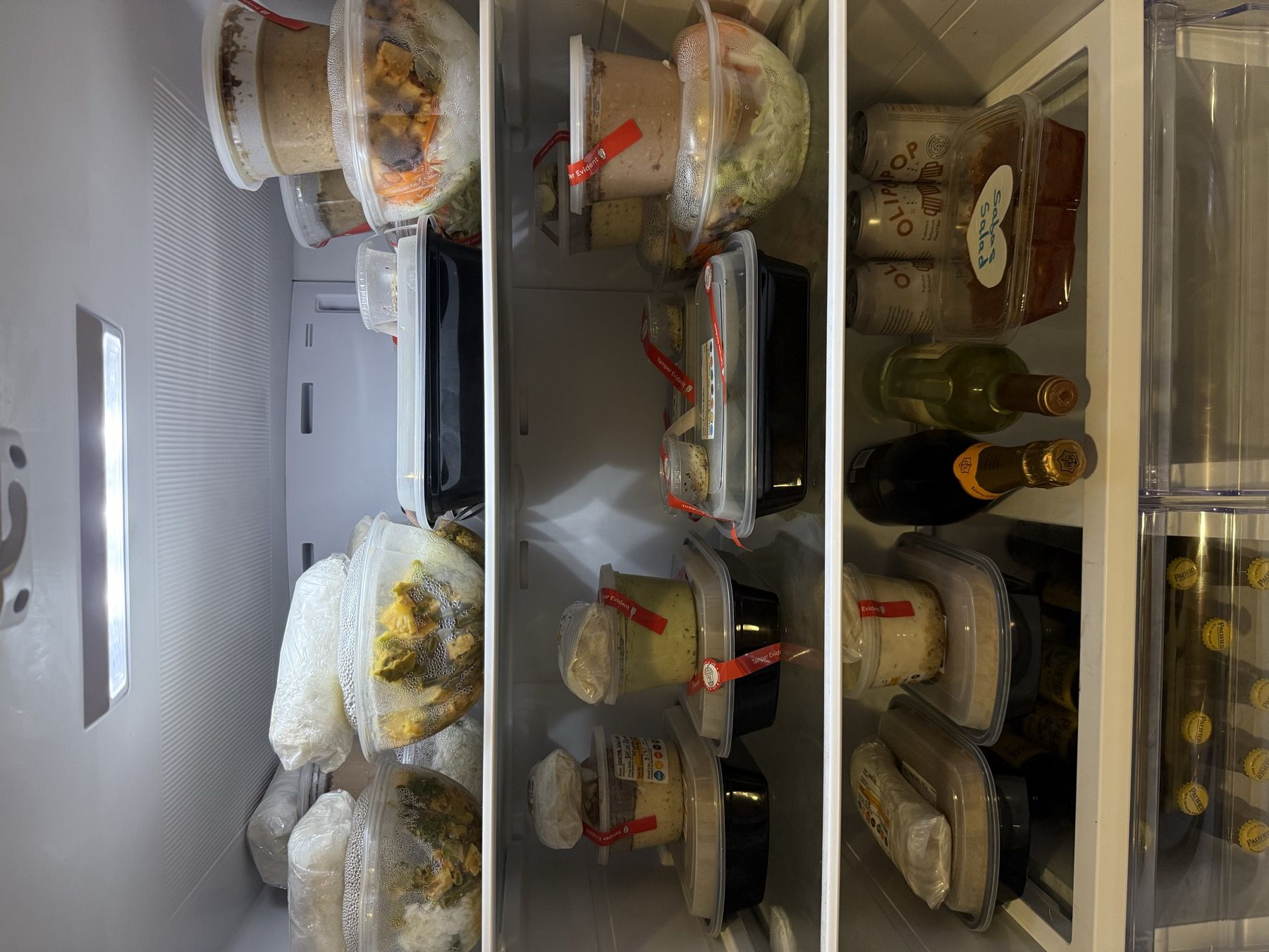 A refrigerator with every shelf stacked with labeled containers